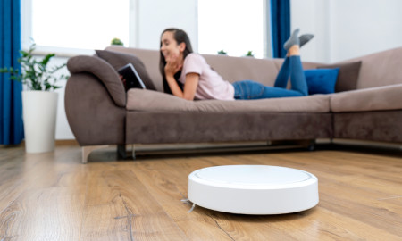 Robotic vacuum cleaner cleaning the room. Woman is lying on the bed. Smart home concept