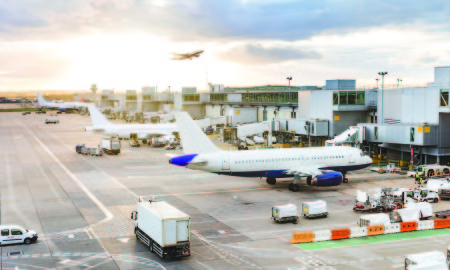 Busy airport view with airplanes and service vehicles at sunset. London airport with aircrafts at gates and taking off, trucks all around and sun setting on background. Travel and industry concepts