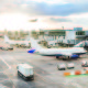 Busy airport view with airplanes and service vehicles at sunset. London airport with aircrafts at gates and taking off, trucks all around and sun setting on background. Travel and industry concepts