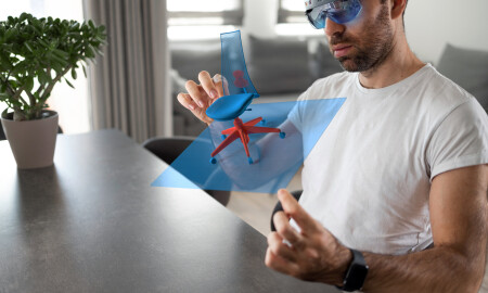 A male furniture designer wears virtual reality glasses and works on a 3D model hologram visualization of an office chair that he is creating.