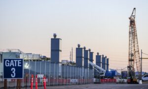 Data center construction site with fenced perimeter, crane, exhaust stacks, and equipment, showing active development of secure technology infrastructure for computing, storage, and network operations