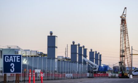 Data center construction site with fenced perimeter, crane, exhaust stacks, and equipment, showing active development of secure technology infrastructure for computing, storage, and network operations