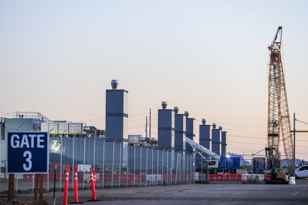 Data center construction site with fenced perimeter, crane, exhaust stacks, and equipment, showing active development of secure technology infrastructure for computing, storage, and network operations